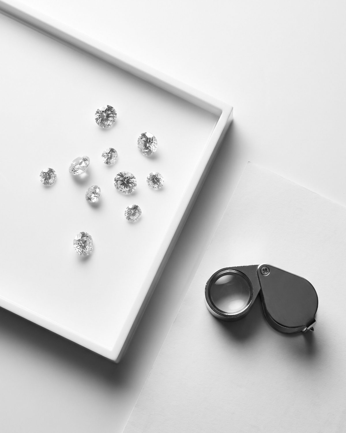 Loose diamonds on a grading tray beside a loupe and a grading report