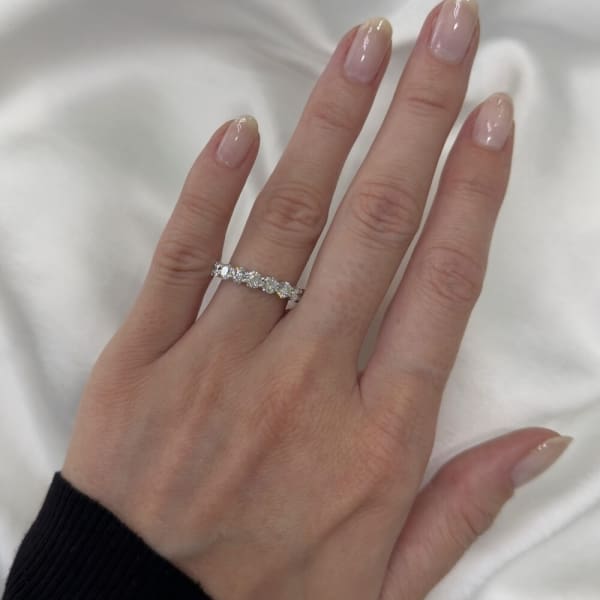 A hand with polished nails adorned with a 1.77ct Round Brilliant Cut Lab Diamond Half Eternity Ring, showcasing a row of sparkling gemstones, resting on a white fabric background.