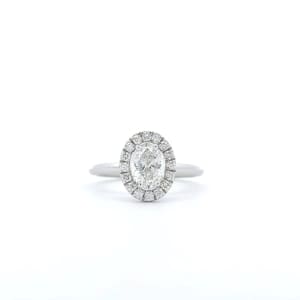 The 1ct Oval Natural Diamond Halo Engagement Ring is showcased on a white background, featuring a stunning silver design with an oval-shaped diamond center stone encircled by a halo of smaller diamonds on a simple band.