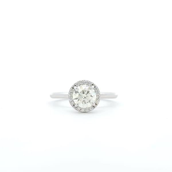 The "1ct Round Brilliant Cut Natural Diamond Halo Engagement Ring" features a large round diamond at its center, encircled by smaller diamonds in an elegant halo setting and is beautifully showcased against a white background.