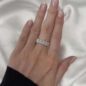 A hand with a black sleeve displays the 3.55ct Oval Lab Diamond Half Eternity Ring, showcasing five large gemstones on a smooth, manicured finger against a backdrop of soft white fabric.