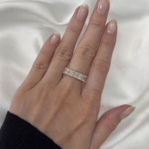 A hand with manicured nails and a black sleeve rests on a white fabric background, showcasing the 3.55ct Radiant Lab Diamond Half Eternity Ring adorned with radiant, rectangular, sparkly gemstones.