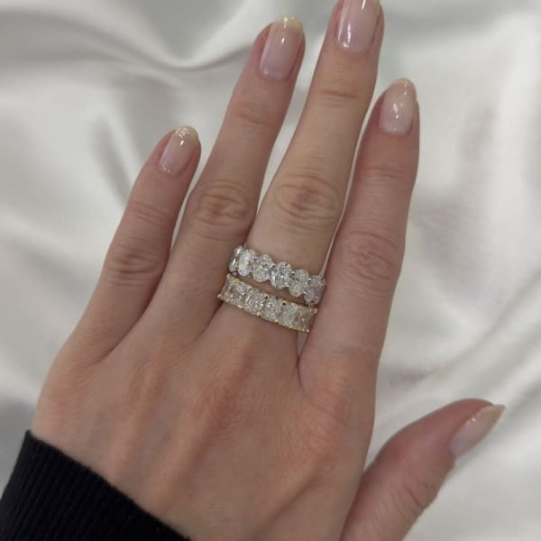 A hand with painted nails wearing a 3.55ct Radiant Lab Diamond Half Eternity Ring on the ring finger, placed on a white satin fabric.