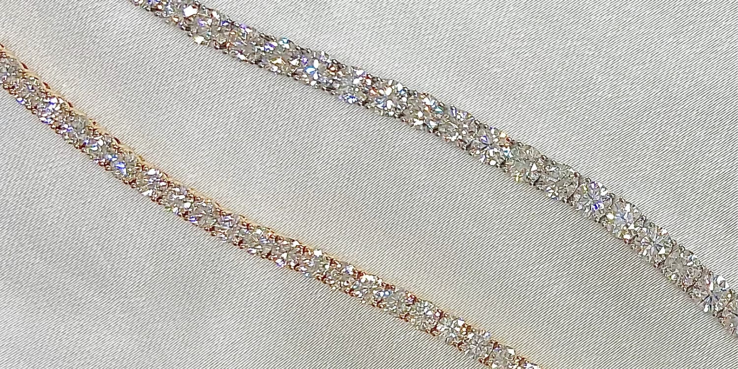 Close-up of two parallel rows of sparkling rhinestones set on a light fabric, reflecting light with a range of colors.