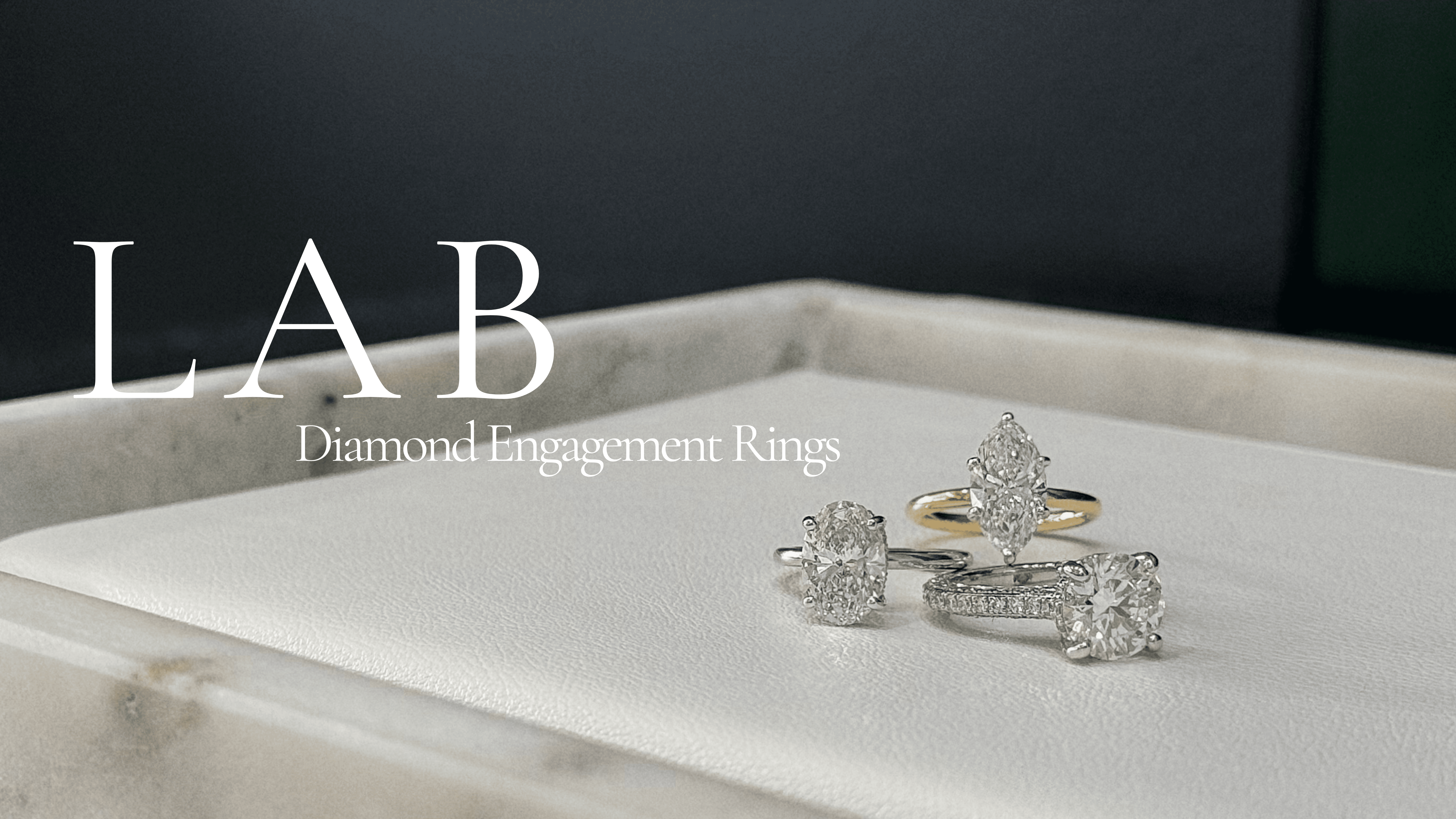 Three diamond engagement rings displayed on a marble surface. One ring has a gold band, while the other two have silver bands. The text "LAB Diamond Engagement Rings" is on the left side of the image.